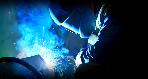 Man wearing a welding mask welding a peice of equipment.